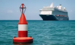 Rote Boje schwimmt im Meer, im Hintergrund unscharf ein großes Kreuzfahrtschiff unter blauem Himmel.