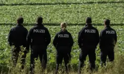 Fünf Polizisten in Uniform stehen auf einem grünen Feld mit dem Rücken zur Kamera und blicken in die Ferne.