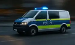 Ein deutscher Polizeibus mit blau-gelber Markierung fährt bei eingeschaltetem Blaulicht auf einer Straße, der Hintergrund ist leicht verschwommen.