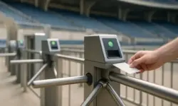 Eine Hand steckt ein Ticket in ein elektronisches Drehkreuz an einem leeren Stadion-Eingang.