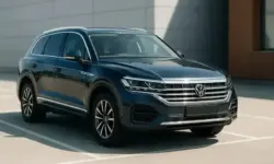 Ein blauer VW Touareg-SUV steht im Sonnenlicht auf einem Parkplatz vor einer Gebäudefassade, fotografiert mit geringer Tiefenschärfe.
