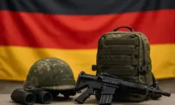 Militärhelm, Fernglas, Rucksack und Gewehr liegen vor einer unscharfen deutschen Flagge.