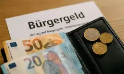 Offene Geldbörse mit Euro-Scheinen und Münzen neben einem Formular mit der Aufschrift „Bürgergeld“.