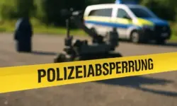 Gelbes Polizeiband mit der Aufschrift „Polizeiabsperrung“ im Vordergrund, dahinter unscharf ein Bombenentschärfungsroboter und ein Polizeifahrzeug.