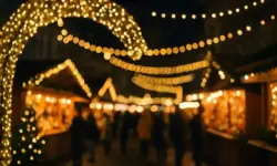 Weihnachtsmarkt bei Nacht mit hell erleuchteten Holzbuden, vielen Lichterketten und unscharfen Besuchern im Vordergrund.