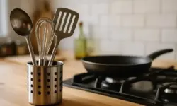 Küchenutensilien in einem Metallhalter neben einer Pfanne auf einem Herd in einer modernen Küche.