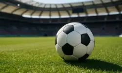Schwarz-weißer Fußball auf grünem Rasen in einem leeren Stadion mit unscharfem Hintergrund.