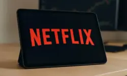 Tablet auf einem Schreibtisch mit großem roten Netflix-Schriftzug auf dem Display, im Hintergrund verschwommene Börsengrafiken.