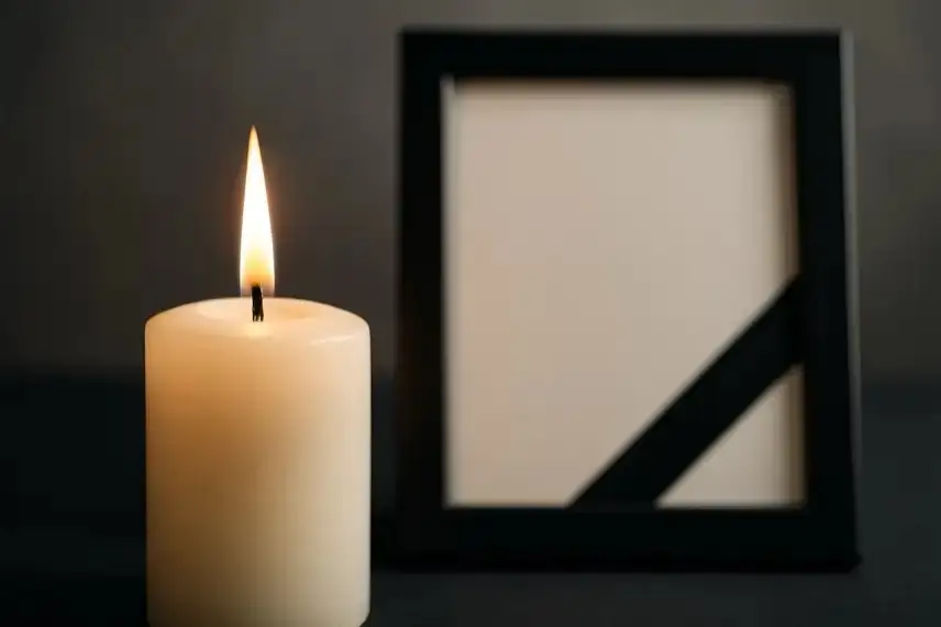 Brennende helle Kerze im Vordergrund, daneben ein unscharfer schwarzer Rahmen mit diagonalem Trauerband.