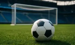 Fußball auf Rasen, im Vordergrund scharf fokussiert, im Hintergrund ein unscharfes Tor in einem leeren Stadion.