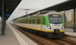 Moderner grüner Regionalzug steht an einem leeren Bahnhof auf geraden Gleisen unter einem überdachten Bahnsteig.