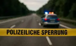 Gelbes Polizei-Absperrband auf einer leeren Autobahn, im Hintergrund ein unscharfes Polizeifahrzeug mit eingeschalteten Blaulichtern.