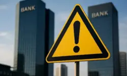 Gelbes Warnschild mit Ausrufezeichen vor zwei unscharfen, hohen Bankgebäuden im Hintergrund.