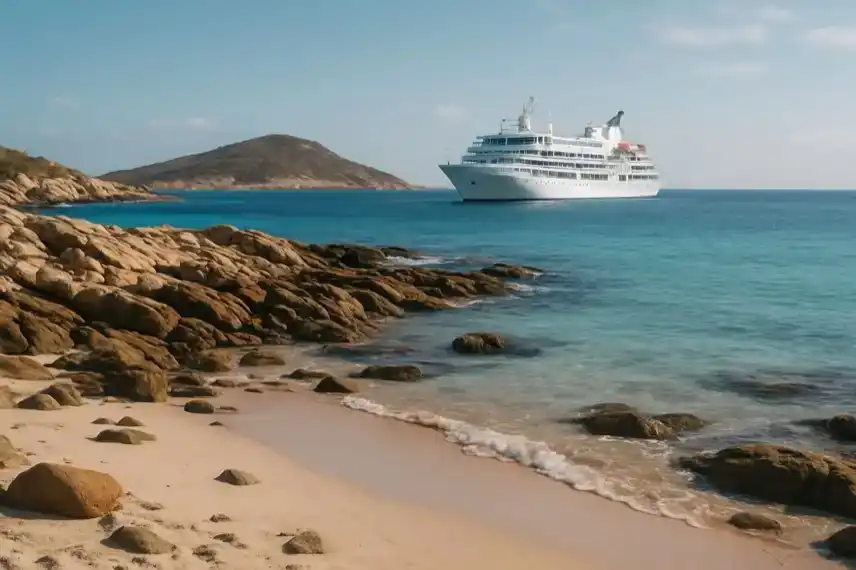 Ein Kreuzfahrtschiff liegt vor einer felsigen tropischen Insel im türkisblauen Meer bei sonnigem Wetter.