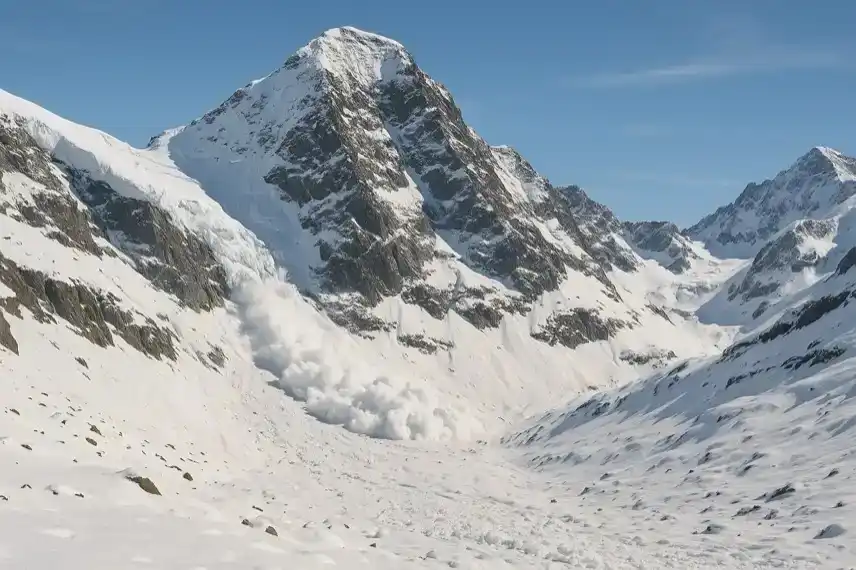 Schneebedecktes Bergmassiv mit einer herabgehenden Lawine im hochalpinen Gelände unter blauem Himmel.