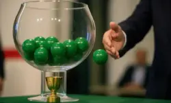 Nahaufnahme einer gläsernen Lostrommel mit grünen Kugeln, aus der eine Hand eine Kugel zieht.