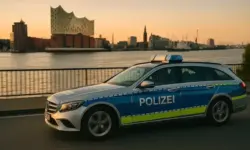 Deutsches Polizeiauto fährt am Elbufer entlang, im Hintergrund die Elbe und Gebäude bei Sonnenuntergang.