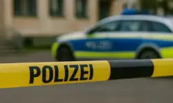 Absperrband mit der Aufschrift „Police Line Do Not Cross“ vor einem unscharfen Gebäude, einem Polizeiwagen und einem verschwommen dargestellten Polizeibeamten.