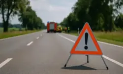 Warnschild auf einer Landstraße, im Hintergrund unscharf ein Einsatzfahrzeug und Einsatzkräfte bei sonnigem Tageslicht.
