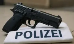 Nahaufnahme einer schwarzen Pistole, die auf einer weißen Armbinde mit der Aufschrift „Polizei“ liegt.