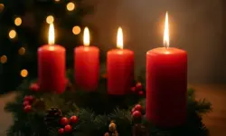 Ein Adventskranz mit vier rot brennenden Kerzen, dekoriert mit Tannenzweigen, Beeren und Zapfen, fotografiert in warmem Licht.