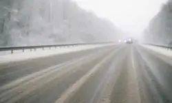 Vereiste, schneebedeckte Autobahn mit Einsatzfahrzeugen im Hintergrund, leicht neblige Winterstimmung ohne erkennbare Fahrzeuge im Vordergrund.