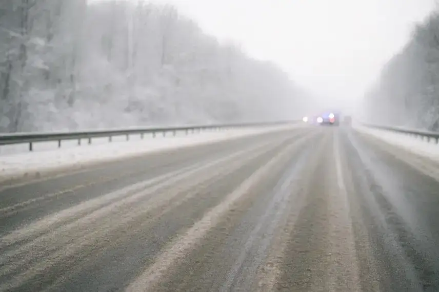 Vereiste, schneebedeckte Autobahn mit Einsatzfahrzeugen im Hintergrund, leicht neblige Winterstimmung ohne erkennbare Fahrzeuge im Vordergrund.