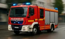 Rotes Feuerwehrauto mit Blaulicht fährt mit hoher Geschwindigkeit über eine nasse Straße in einer Stadt.