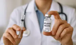 Nahaufnahme eines medizinischen Stilllebens mit Impfstoffvial und Spritze auf weißem Tisch, hell ausgeleuchtet und ohne Menschen.