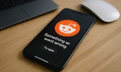 Ein Smartphone liegt auf einem Holztisch und zeigt eine Reddit-Fehlermeldung auf dem Bildschirm, daneben eine Computermaus.