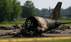 Verbranntes Flugzeugwrack liegt auf einer offenen Fläche mit gelbem Absperrband und Industriegebäuden im Hintergrund.