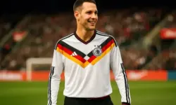 Mann mit kurzem Haar trägt das weiße DFB-Trikot mit schwarz-rot-goldenem V-Muster, steht lächelnd im Stadion.