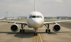 Shutdown: Frontansicht eines weißen Passagierflugzeugs auf dem Rollfeld bei Tageslicht, Hintergrund mit weiteren Flugzeugen und Hangars.
