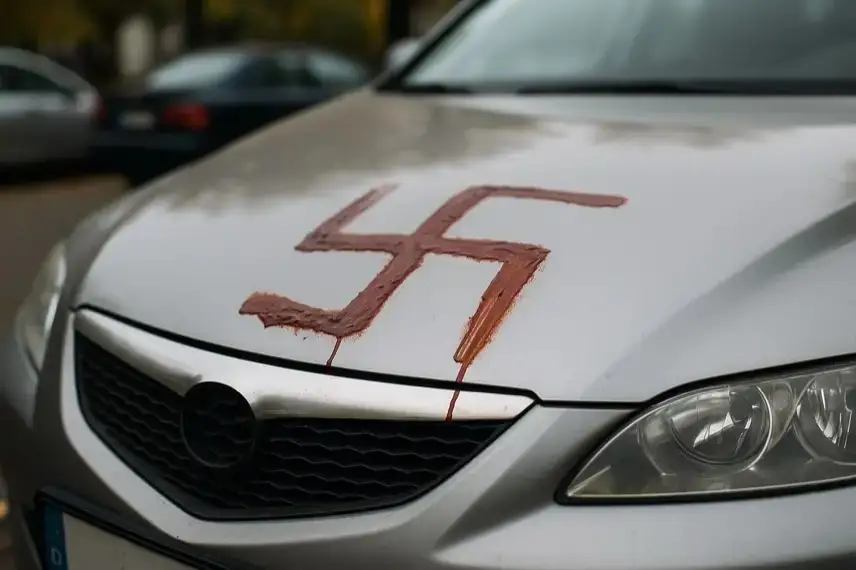Nahaufnahme einer Autokarosserie mit einem aufgemalten Hakenkreuz, aufgenommen bei Tageslicht, ohne erkennbare Personen.