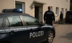 Ein Polizeiauto mit der Aufschrift „Polizei“ steht vor einem Wohnhaus, während zwei Beamte in Uniform vor dem Gebäude stehen.