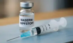 Nahaufnahme einer Spritze und eines Impfstoff-Fläschchens mit der Aufschrift „Masern-Impfstoff“ auf einem hellen Untergrund.