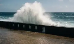Hohe Welle bricht über eine Meeresmauer an einer sonnigen Küstenpromenade.