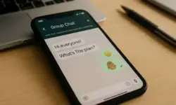 Smartphone auf Holztisch mit geöffneter WhatsApp-Chatansicht, daneben ein Laptop und ein Stift.