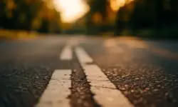 Asphaltstraße mit Mittelstreifen, aufgenommen aus Bodennähe bei warmem Sonnenlicht, Hintergrund unscharf mit Bäumen.