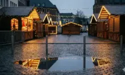 Leerer Weihnachtsmarkt bei Dämmerung mit beleuchteten Buden, Lichterketten, Metallpollern und nassem Kopfsteinpflaster.