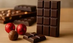 Hochwertige Schokoladentafeln und Pralinen auf einer edlen Oberfläche, im Hintergrund unscharf angedeutete Supermarktregale ohne Beschriftung.