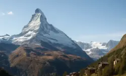 Moderne Hochhaus-Silhouette vor schneebedeckter alpiner Berglandschaft bei Tageslicht.