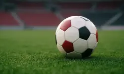 Leerer Fußballplatz mit einem einzelnen Spielball auf grünem Rasen, unscharfe Stadiontribüne im Hintergrund, aufgenommen bei natürlichem Licht.