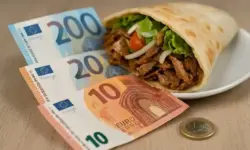 Döner im Fladenbrot auf einem Teller, daneben Euro-Banknoten und eine Euromünze auf einer Holzoberfläche.