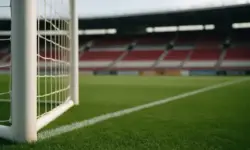 Leeres Fußballstadion mit grünem Rasen, weißem Torpfosten und Tornetz im Vordergrund.