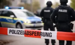 Polizeisperrband mit der Aufschrift „Polizeiabsperrung“, dahinter unscharf ein Polizeifahrzeug mit Blaulicht und zwei Einsatzkräfte.
