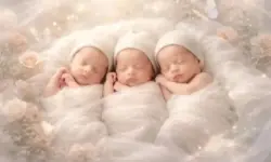 Drei schlafende, identisch aussehende Babys liegen nebeneinander auf hellem, weichem Untergrund in einer künstlerischen Darstellung.