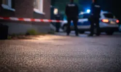 Nächtliche Straßenszene mit nassem Pflaster und unscharfen blauen und roten Lichtreflexionen vor einem anonymen Gebäudeeingang.