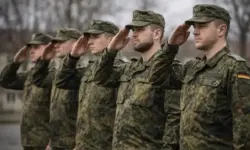 Fünf Bundeswehrsoldaten in Flecktarn-Uniform stehen in einer Reihe im Freien und salutieren synchron bei einer militärischen Zeremonie