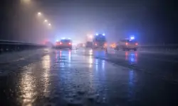 Vereiste Autobahn bei Nacht mit Nebel, stehenden Fahrzeugen und Blaulicht nach einem Unfall auf spiegelglatter Fahrbahn